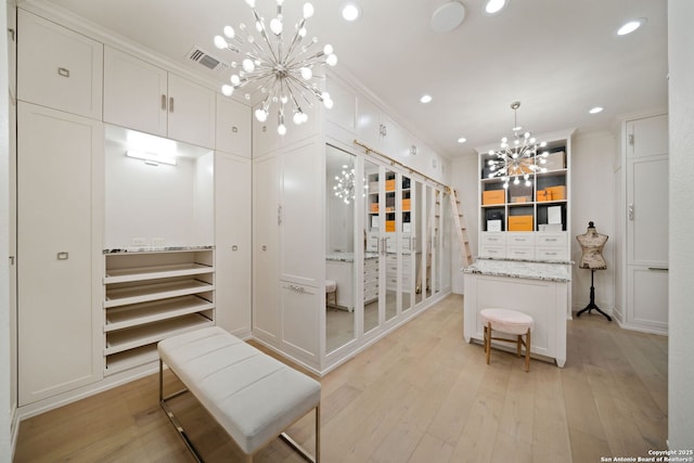 walk in closet with light wood-type flooring, visible vents, and an inviting chandelier