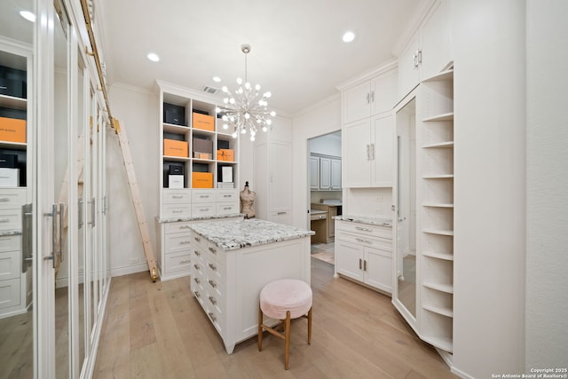 walk in closet with light wood finished floors and an inviting chandelier