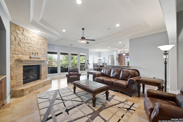 living area featuring ornamental molding, a stone fireplace, a raised ceiling, and recessed lighting