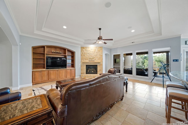 living room featuring a fireplace, a ceiling fan, baseboards, a tray ceiling, and crown molding