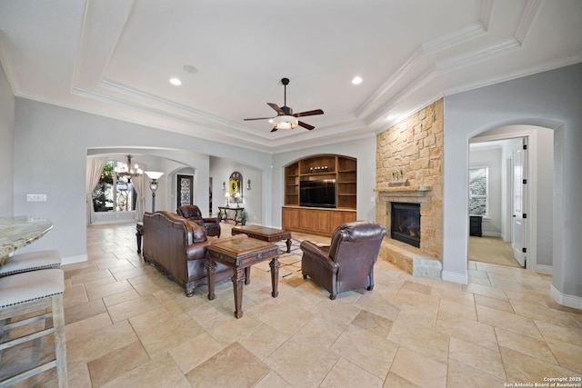 living area featuring baseboards, built in features, a raised ceiling, ornamental molding, and a fireplace