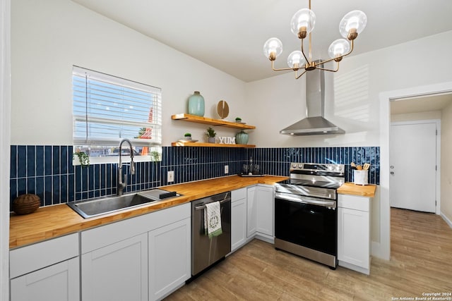 kitchen featuring appliances with stainless steel finishes, a sink, wood counters, light wood-type flooring, and wall chimney exhaust hood