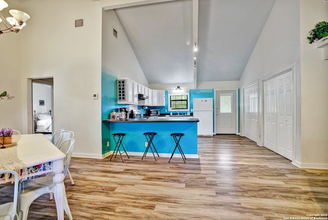 kitchen with light wood finished floors, visible vents, freestanding refrigerator, a peninsula, and a kitchen bar