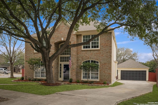 traditional-style home featuring a shingled roof, a detached garage, a front lawn, and brick siding