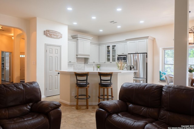 living area with arched walkways, light tile patterned floors, recessed lighting, visible vents, and baseboards