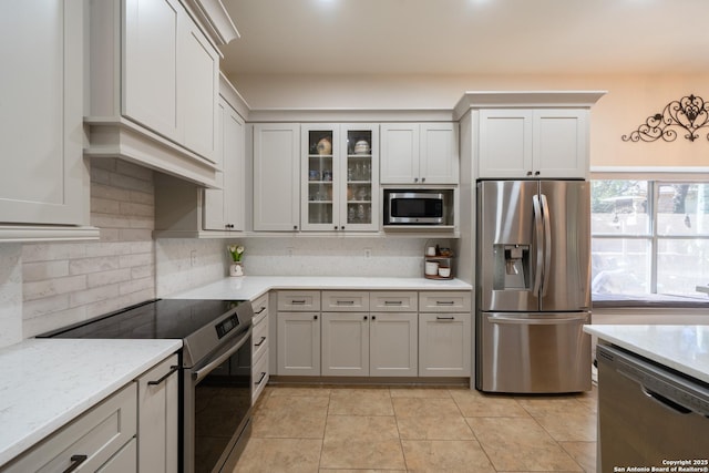 kitchen with glass insert cabinets, light stone countertops, appliances with stainless steel finishes, and backsplash