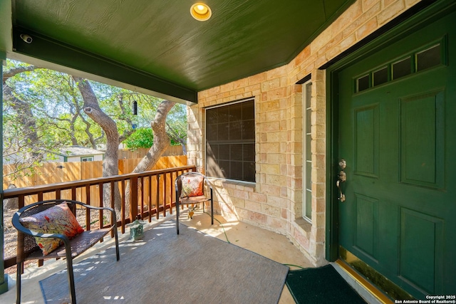 property entrance with a porch, stone siding, and fence