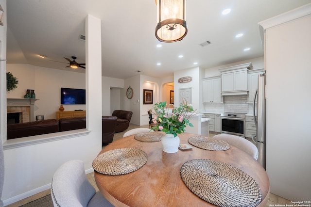 dining space with ceiling fan, arched walkways, recessed lighting, a fireplace, and visible vents