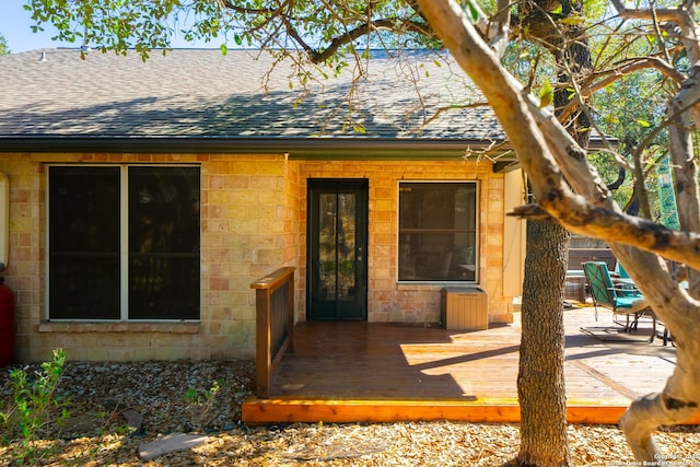 property entrance featuring roof with shingles and a wooden deck