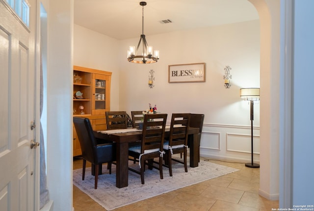 dining room with arched walkways, wainscoting, a chandelier, a decorative wall, and light tile patterned flooring