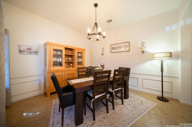 dining room with a notable chandelier, light tile patterned floors, visible vents, a decorative wall, and wainscoting