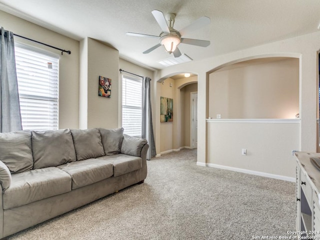 living room featuring arched walkways, light colored carpet, visible vents, baseboards, and a ceiling fan