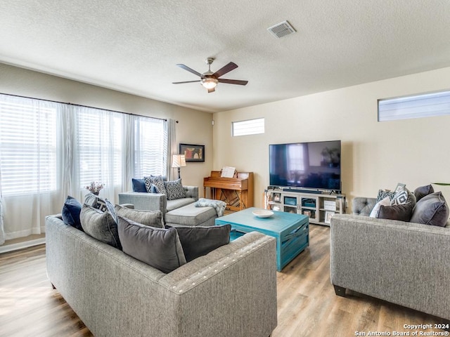 living room with ceiling fan, light wood finished floors, a textured ceiling, and visible vents