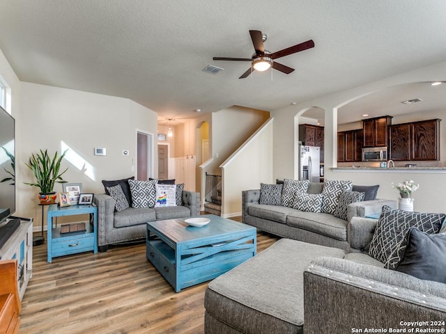 living area with light wood finished floors, visible vents, ceiling fan, a textured ceiling, and stairs