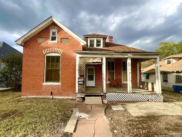 view of front of house featuring covered porch, brick siding, and a chimney