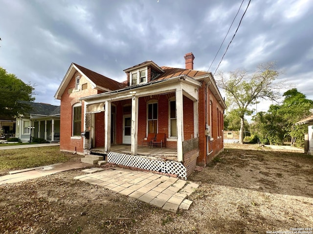 view of front facade with covered porch, brick siding, and a chimney