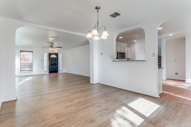 unfurnished living room featuring arched walkways, recessed lighting, ceiling fan with notable chandelier, visible vents, and light wood-style floors