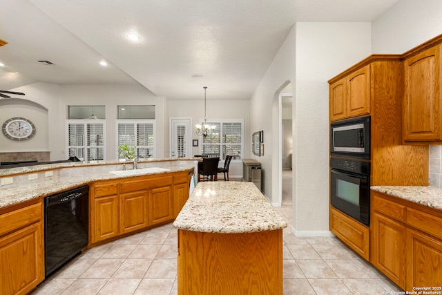 kitchen with black appliances, brown cabinets, a center island, and light stone countertops