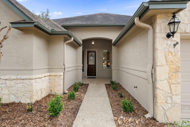 doorway to property with an attached garage, stone siding, and a shingled roof