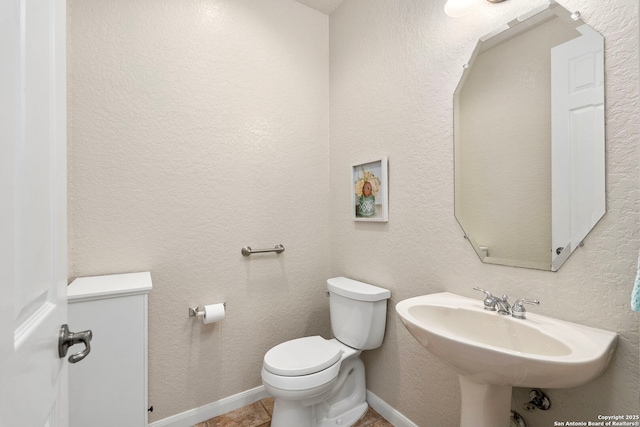 half bathroom with a textured wall, toilet, a sink, baseboards, and tile patterned floors