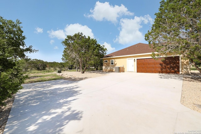 view of home's exterior featuring an attached garage, cooling unit, concrete driveway, and stucco siding