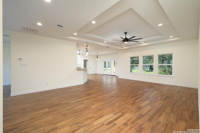 unfurnished living room featuring light wood finished floors, a tray ceiling, and visible vents