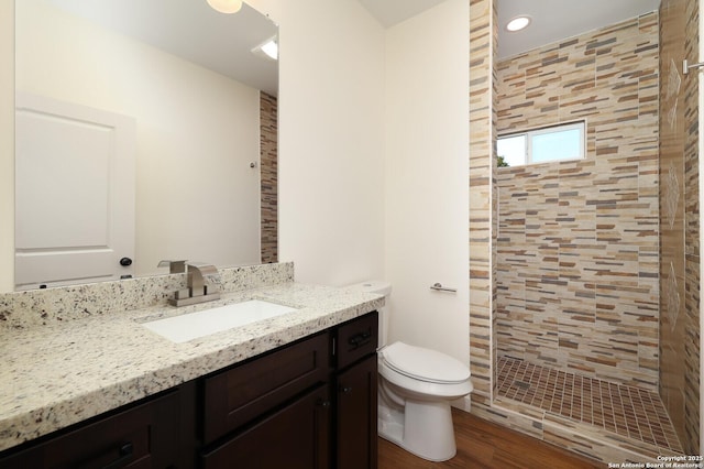 bathroom featuring toilet, wood finished floors, tiled shower, and vanity