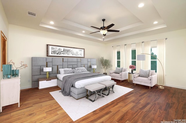 bedroom with a raised ceiling, visible vents, baseboards, and wood finished floors