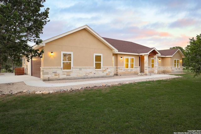 back of house at dusk with a yard, stucco siding, concrete driveway, a garage, and stone siding