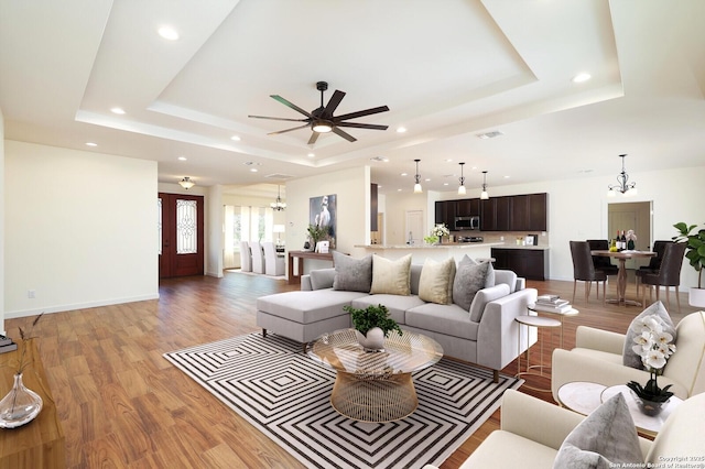 living room featuring light wood finished floors, visible vents, baseboards, and a raised ceiling