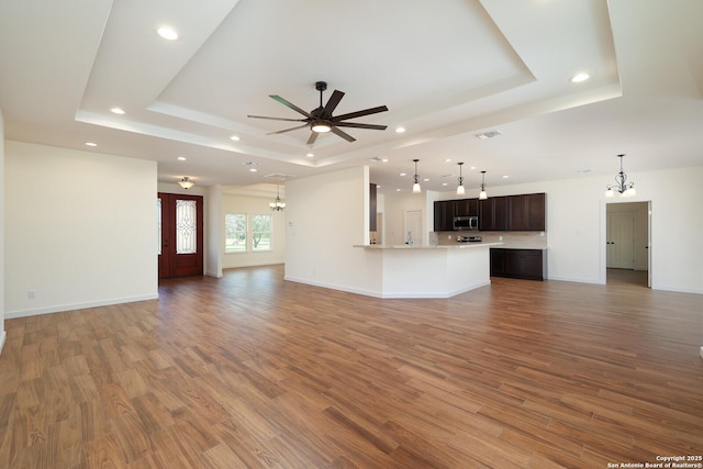 unfurnished living room featuring baseboards, a raised ceiling, wood finished floors, and ceiling fan with notable chandelier