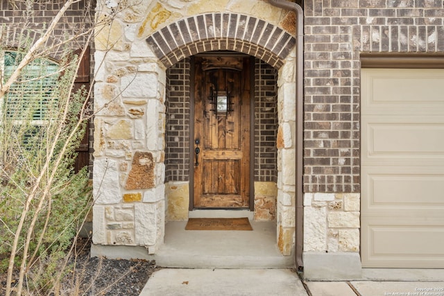 view of exterior entry featuring a garage, stone siding, and brick siding