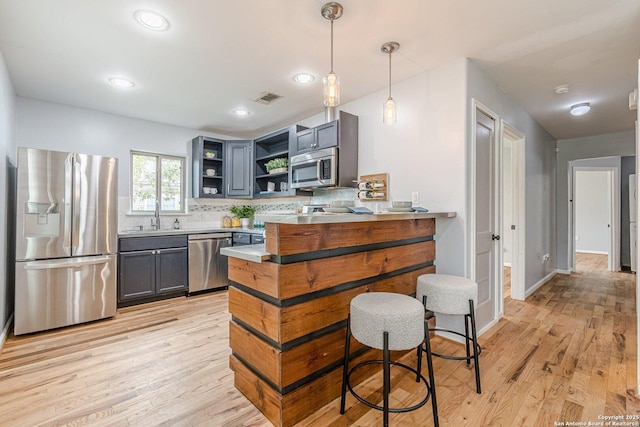 kitchen featuring open shelves, stainless steel appliances, decorative backsplash, light wood-style floors, and a sink