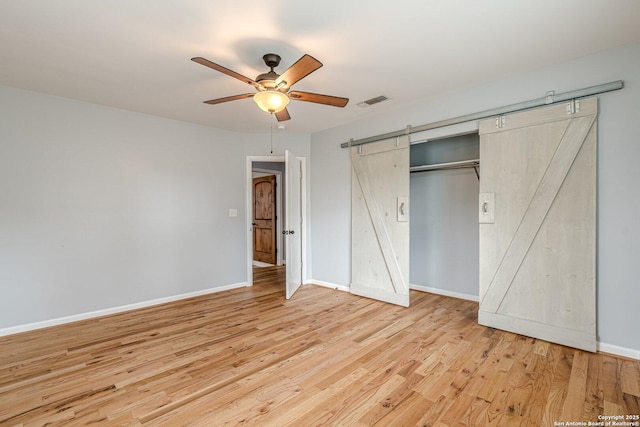 unfurnished bedroom with a barn door, wood finished floors, visible vents, and baseboards