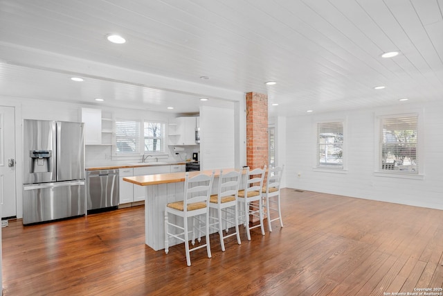 kitchen with a breakfast bar area, open shelves, stainless steel appliances, dark wood-type flooring, and a sink