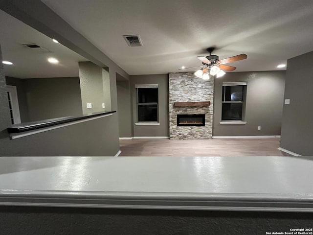 unfurnished living room featuring ceiling fan, a fireplace, wood finished floors, and visible vents