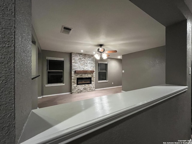 living room with baseboards, visible vents, a ceiling fan, wood finished floors, and a fireplace