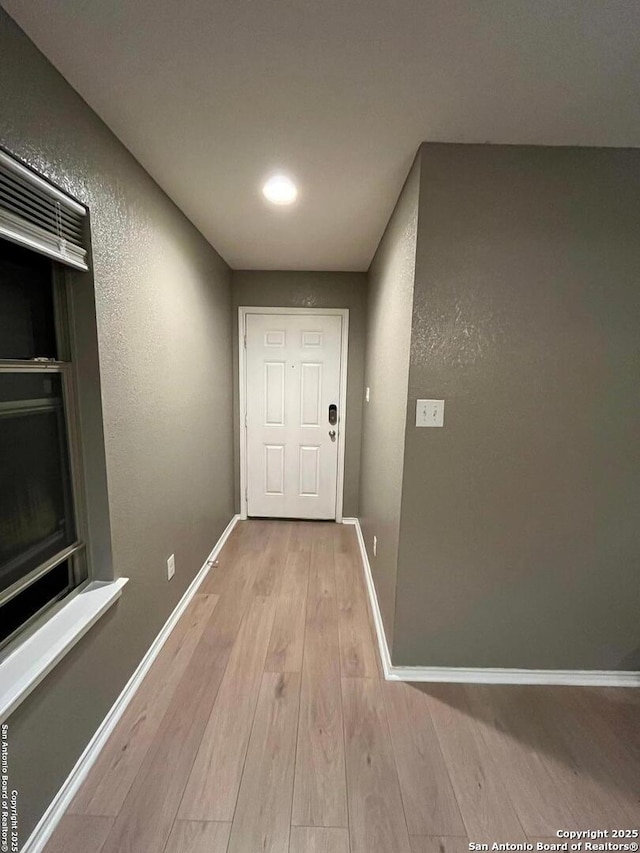 corridor featuring baseboards, wood finished floors, and a textured wall