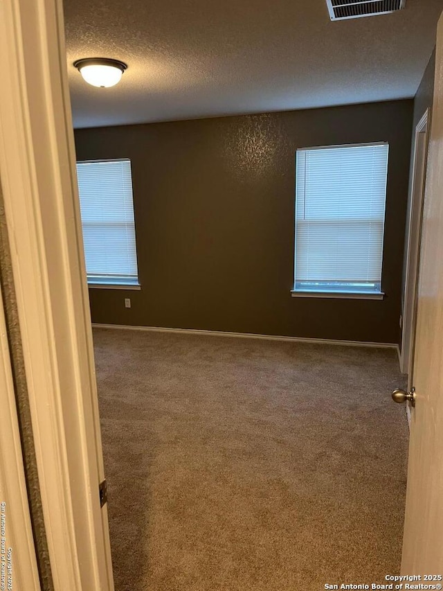 carpeted spare room with a textured ceiling, visible vents, and baseboards