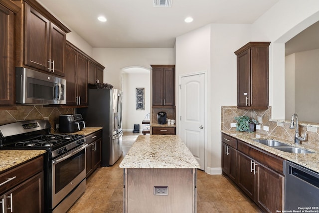 kitchen with arched walkways, stainless steel appliances, a sink, dark brown cabinets, and light stone countertops