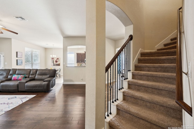 stairway featuring arched walkways, hardwood / wood-style flooring, ceiling fan with notable chandelier, visible vents, and baseboards