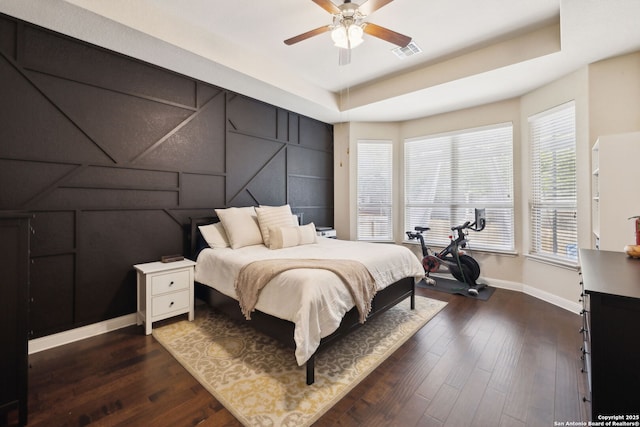 bedroom with a tray ceiling, visible vents, and dark wood-type flooring