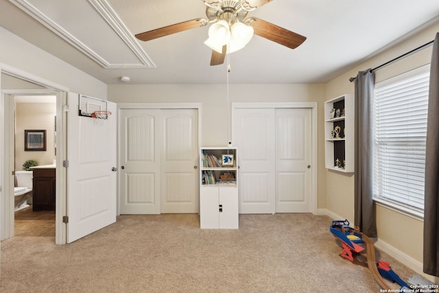 unfurnished bedroom featuring light carpet, attic access, baseboards, a ceiling fan, and multiple closets