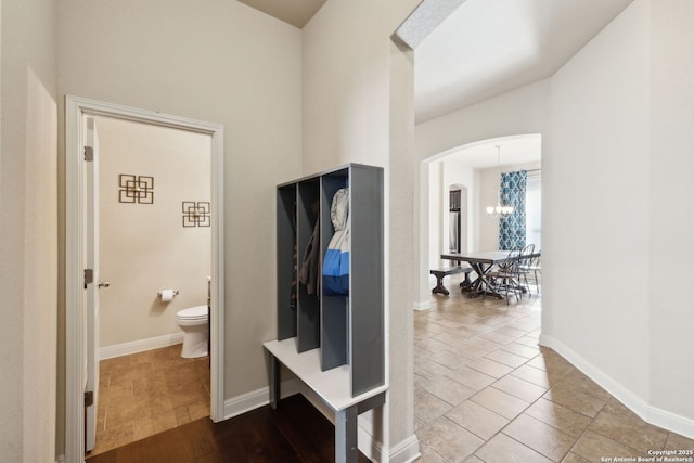 hallway featuring arched walkways, a notable chandelier, and baseboards