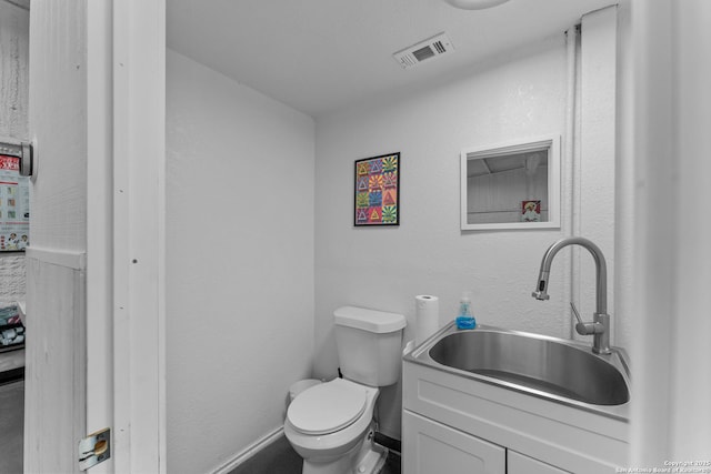 half bath featuring toilet, baseboards, visible vents, and vanity