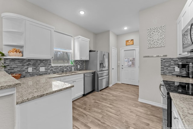 kitchen featuring light wood finished floors, white cabinets, light stone counters, appliances with stainless steel finishes, and a sink