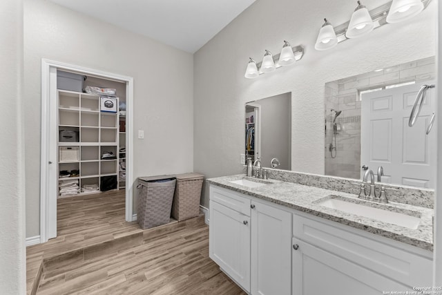 full bath featuring a spacious closet, a tile shower, a sink, and wood finished floors