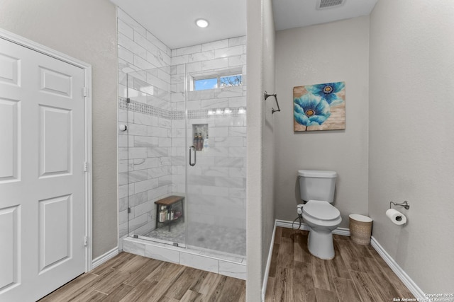 bathroom with toilet, a stall shower, baseboards, and wood finished floors