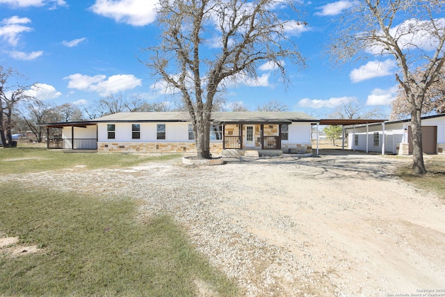 single story home with stone siding, dirt driveway, a front lawn, and an attached carport