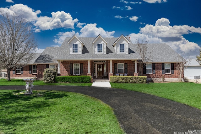 cape cod house featuring covered porch, roof with shingles, brick siding, and a front lawn